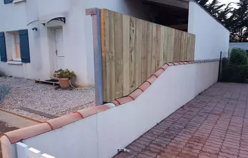 Réalisation d’une clôture en pin traité non raboté type « palissage de chantier ». Pose fixée sur muret. 